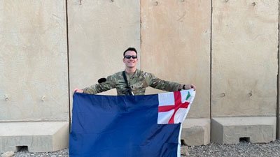 Cameron McMillan with the Charlestown flag in front of some blast walls at Al Asad, Iraq. Photo courtesy of the author.