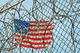 Tattered American flag behind the barbed wire fence of a prison