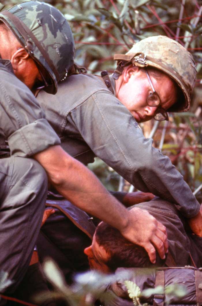 A badly wounded infantryman is attended by a medic and comforted by his battalion commander. 