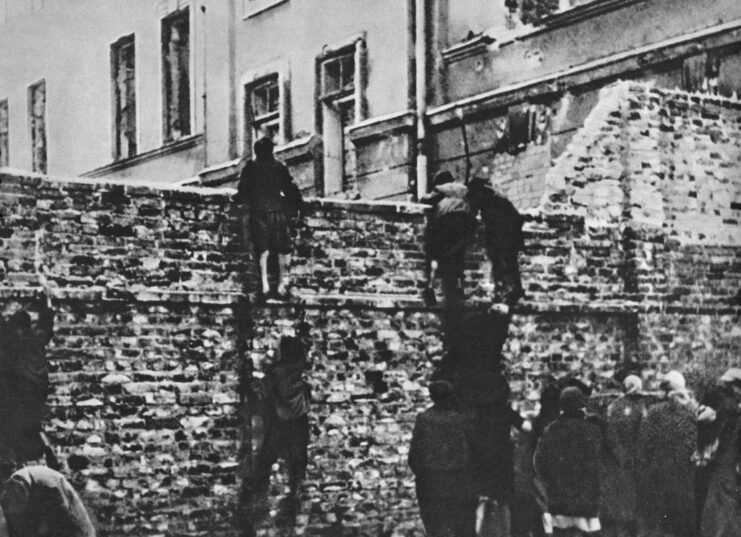 People looking over a brick wall that served as one of the borders of the Warsaw Ghetto